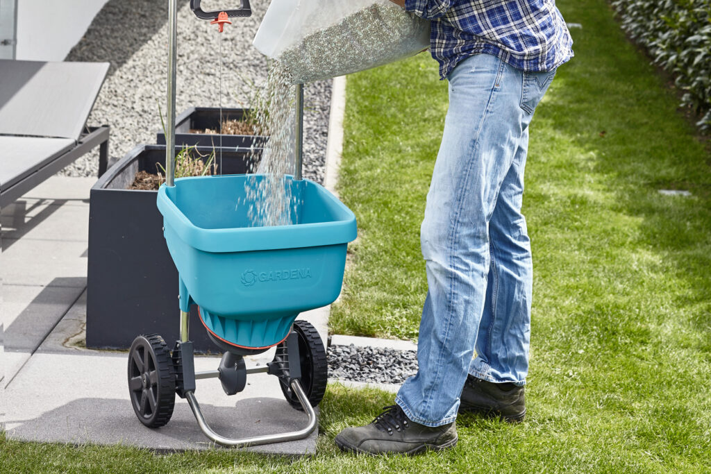 A GARDENA Fertiliser Spreader XL being filled with granulated fertiliser.