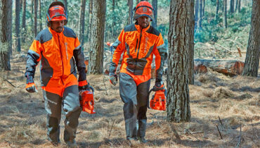 A forester wearing safety gear cuts the branches off a fallen tree with a Husqvarna chainsaw