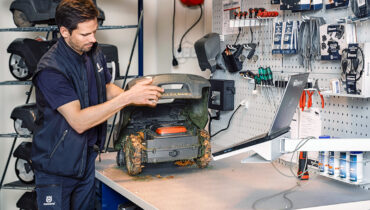 A man servicing a Husqvarna 430 Automower in a workshop.
