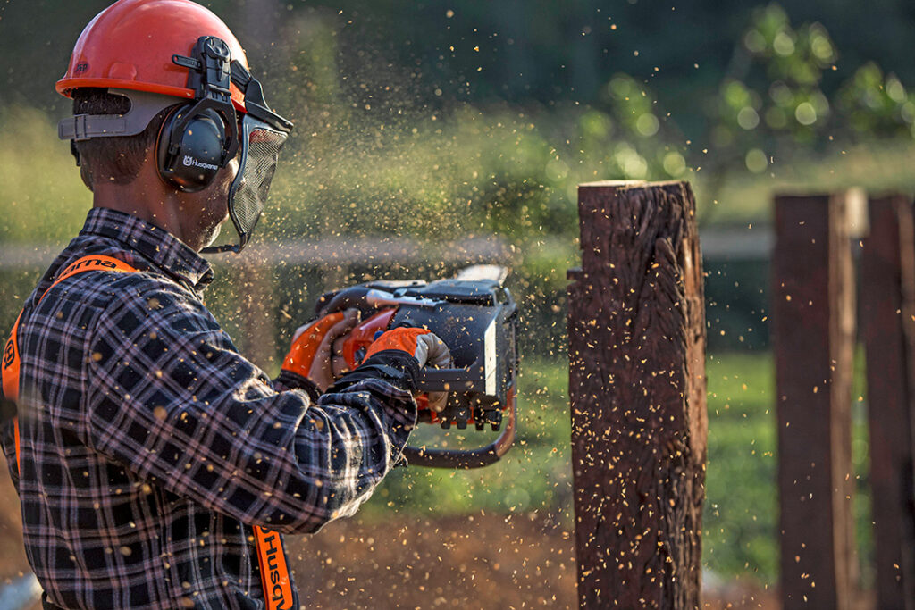 A man uses a Husqvarna battery chainsaw to cut fence poles on a farm.