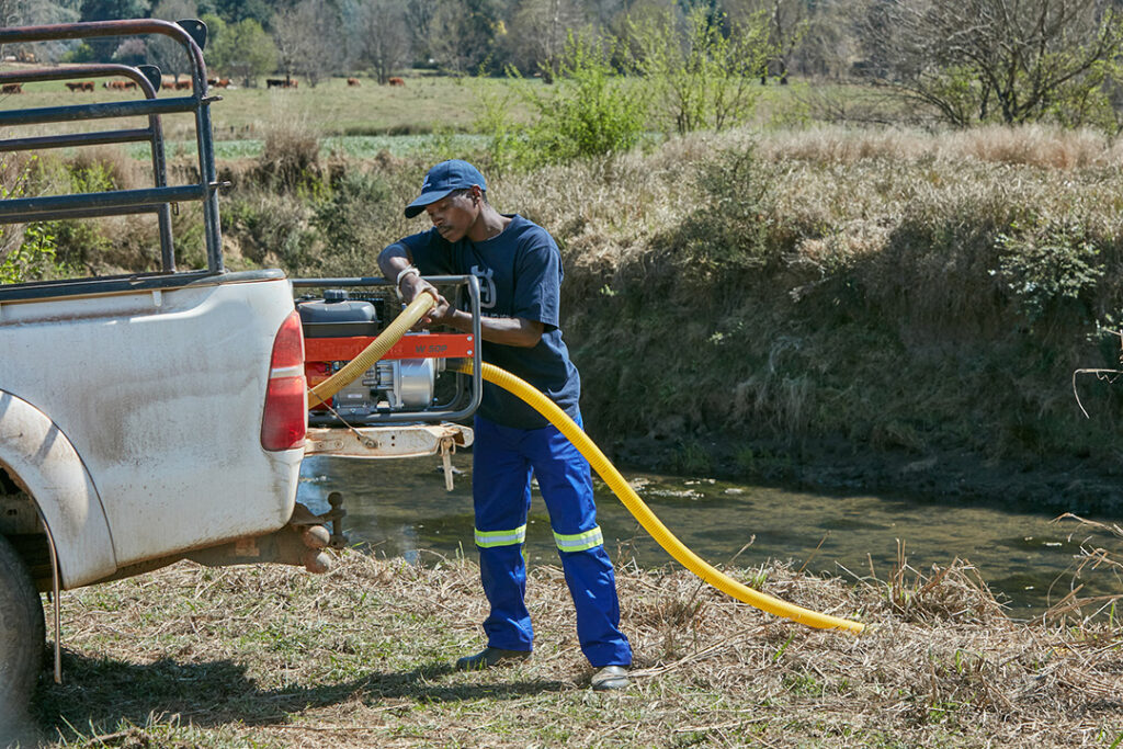 A man pumping water with a Husqvarna W50P water pump in the back of his pick-up truck.