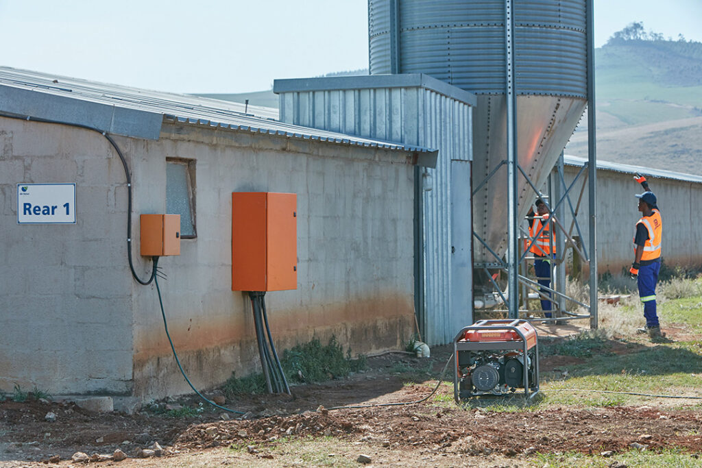 A Husqvarna G5500P generator on the floor outside a farm building with a grain silo in the background.