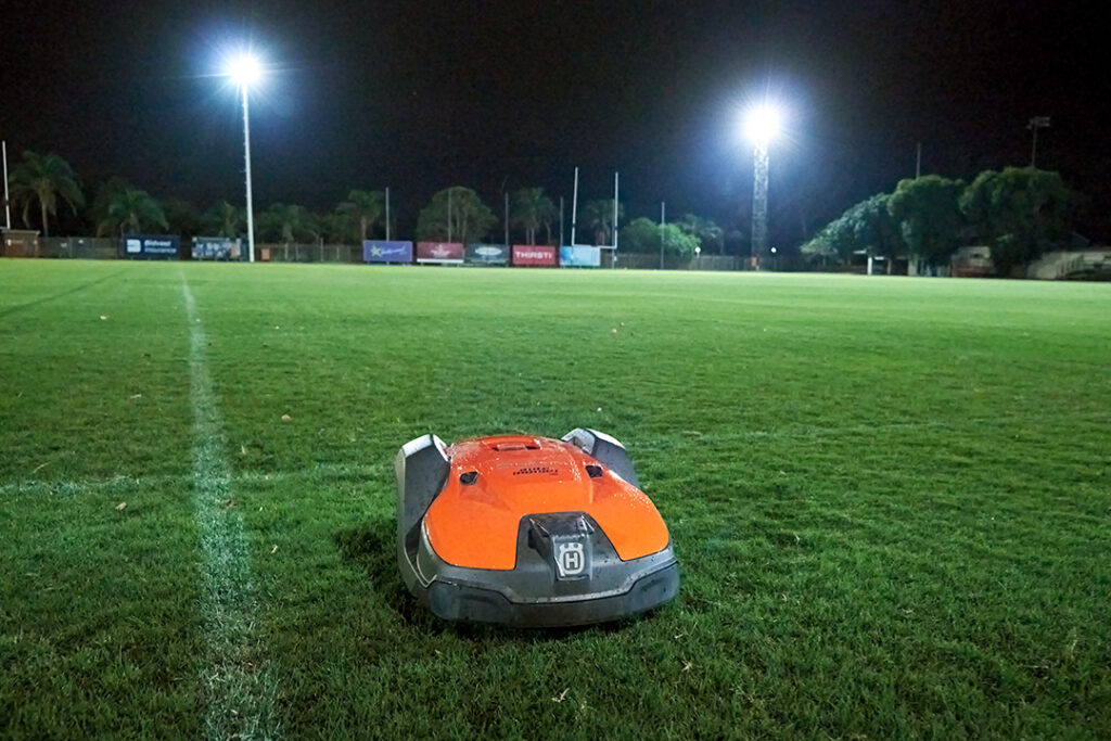 A Husqvarna 550 EPOS Automower working at night on a rugby field under the spotlights.