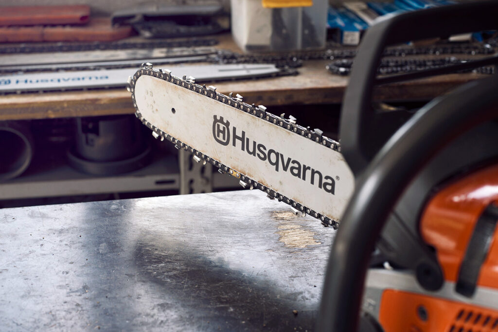 A close-up of a Husqvarna chainsaw guide bar and chain attached to a chainsaw in a workshop.