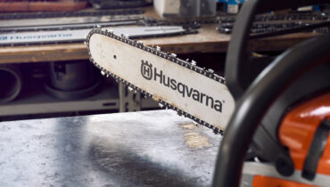 A close-up of a Husqvarna chainsaw guide bar and chain attached to a chainsaw in a workshop.