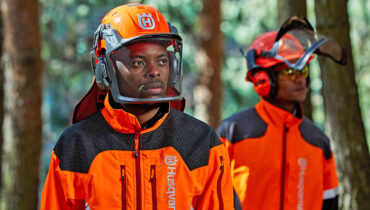 Two foresters wearing Husqvarna PPE forestry helmets and high-visibility jackets.