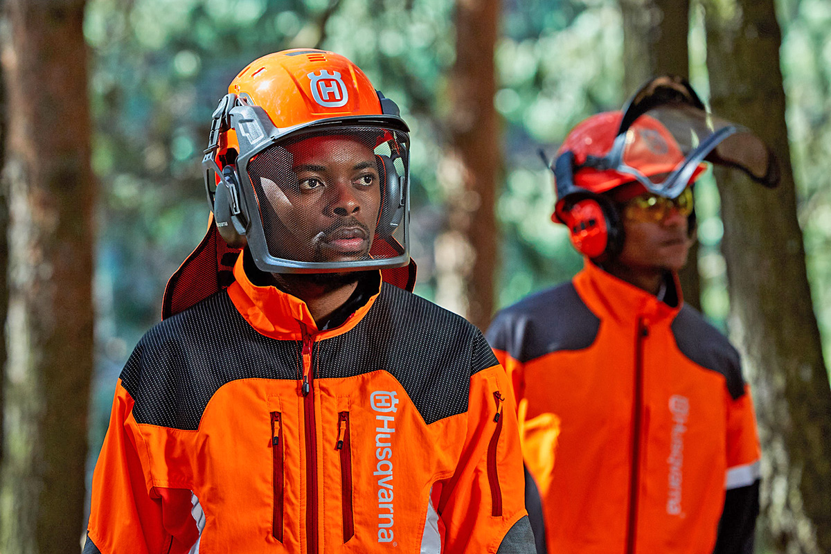 Two foresters wearing Husqvarna PPE forestry helmets and high-visibility jackets.
