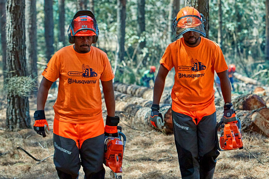 Two foresters wearing Husqvarna PPE forestry helmets and high-visibility jackets.