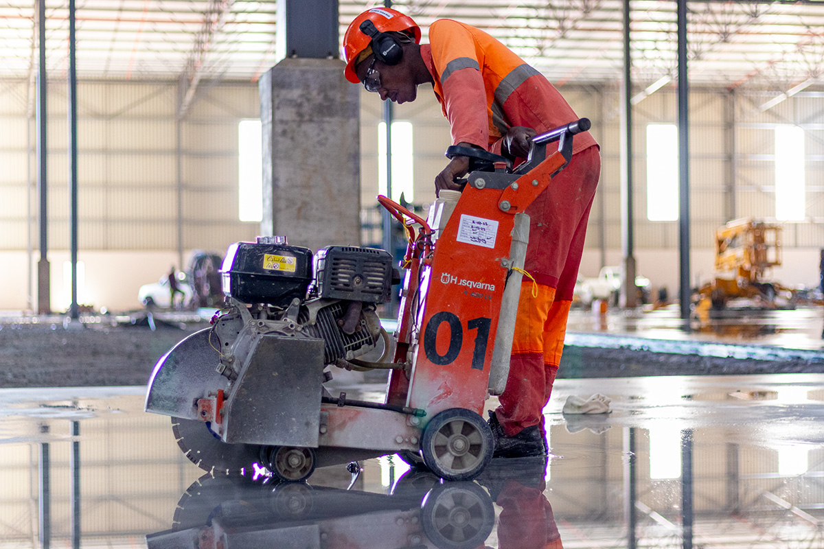 A construction worker operating a Husqvarna floor saw on a freshly poured concrete surface.