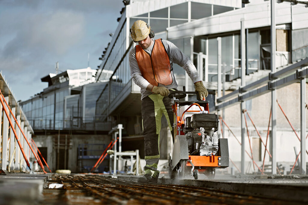 A man pushing a Husqvarna floor saw along a concrete floor on a construction site.