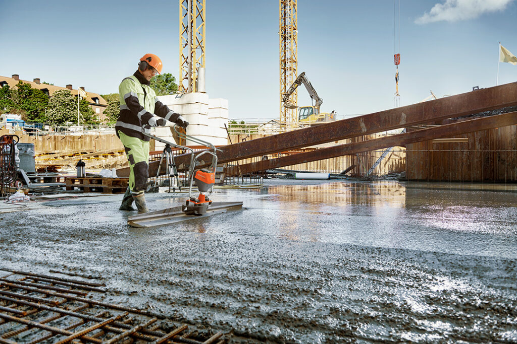 A man using a motorised screeder on fresh concrete.