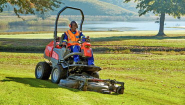 A golf course groundskeeper driving a Husqvarna ride on mower across a fairway.
