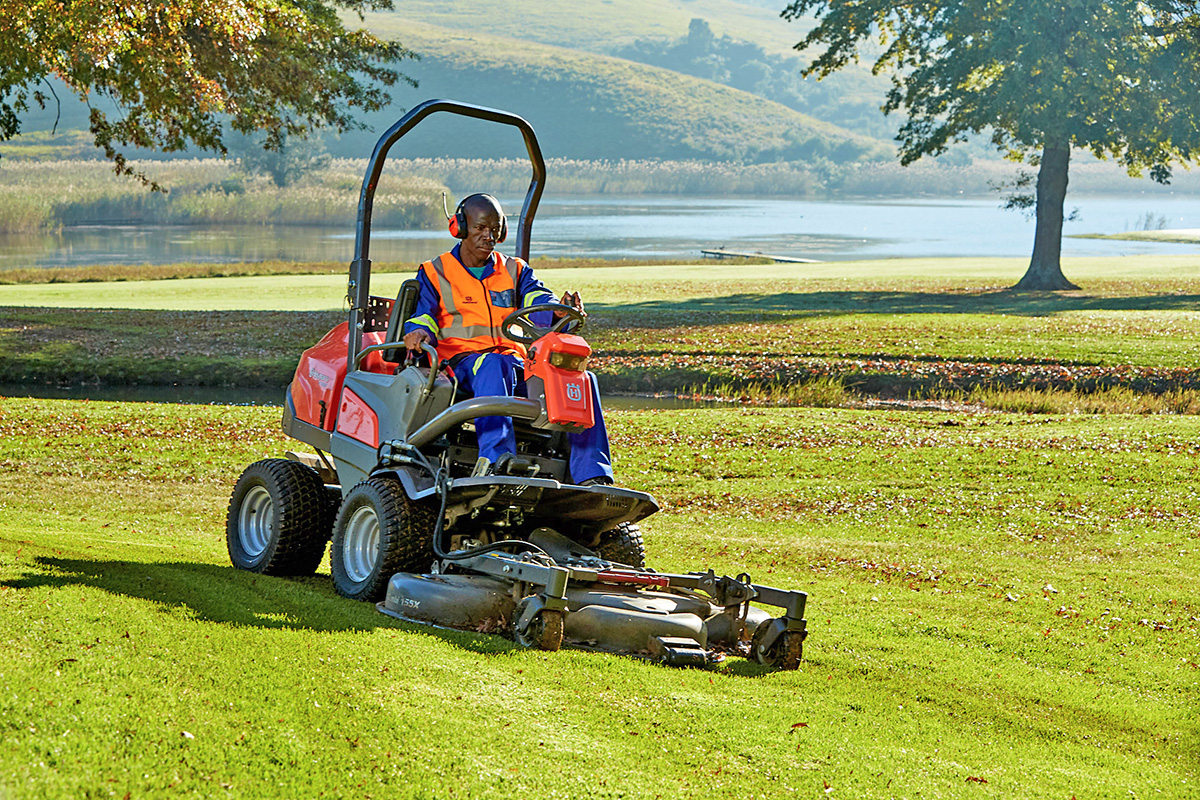 A golf course groundskeeper driving a Husqvarna ride on mower across a fairway.