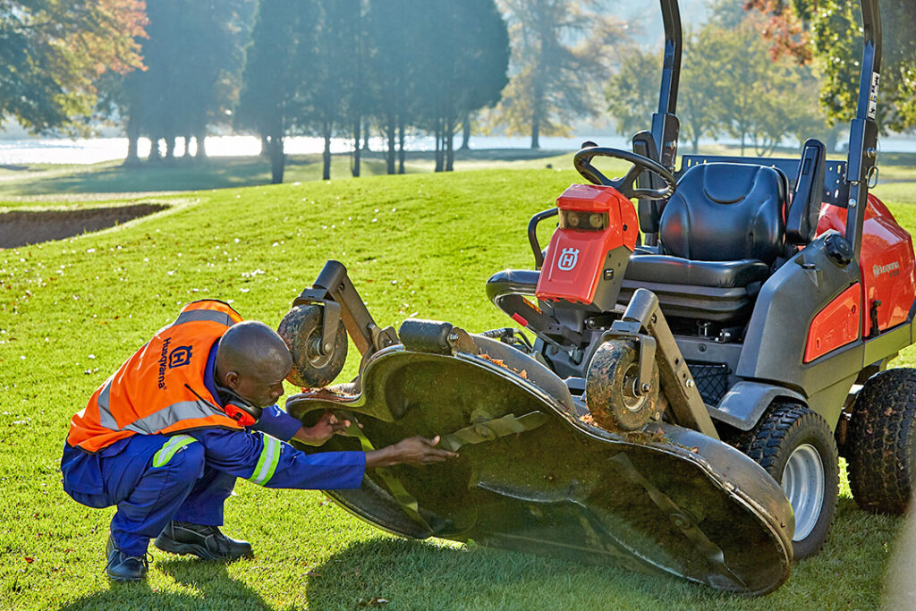 A groundskeeper inspecting the cutting blades on a Husqvarna ride on mower.