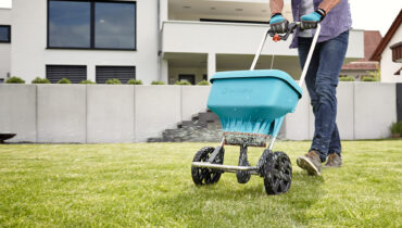 A man pushing a GARDENA Fertiliser Spreader to dispense granulated fertiliser on his green lawn.