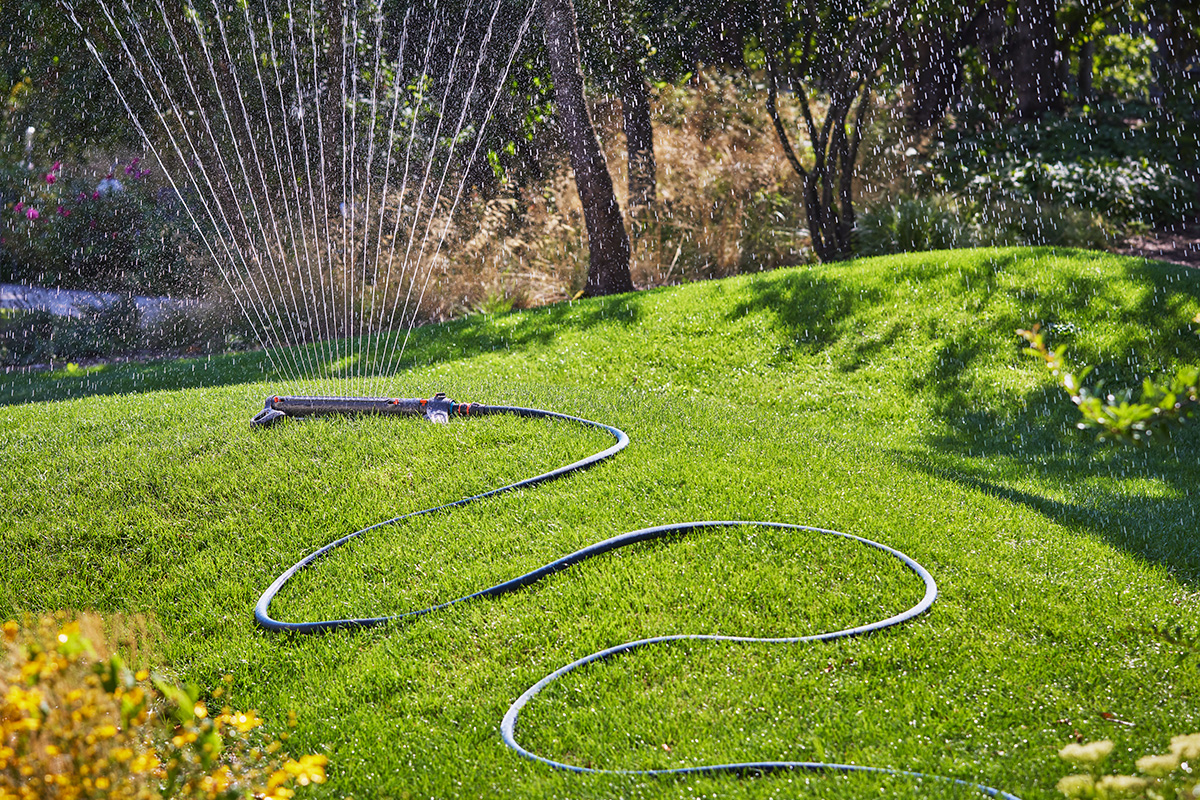 A GARDENA Oscillating Sprinkler on a green lawn with a blue hose pipe.