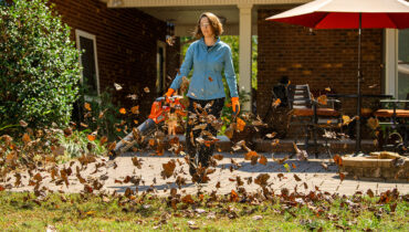 A lady using a Husqvarna leaf blower to remove leaves from her patio.