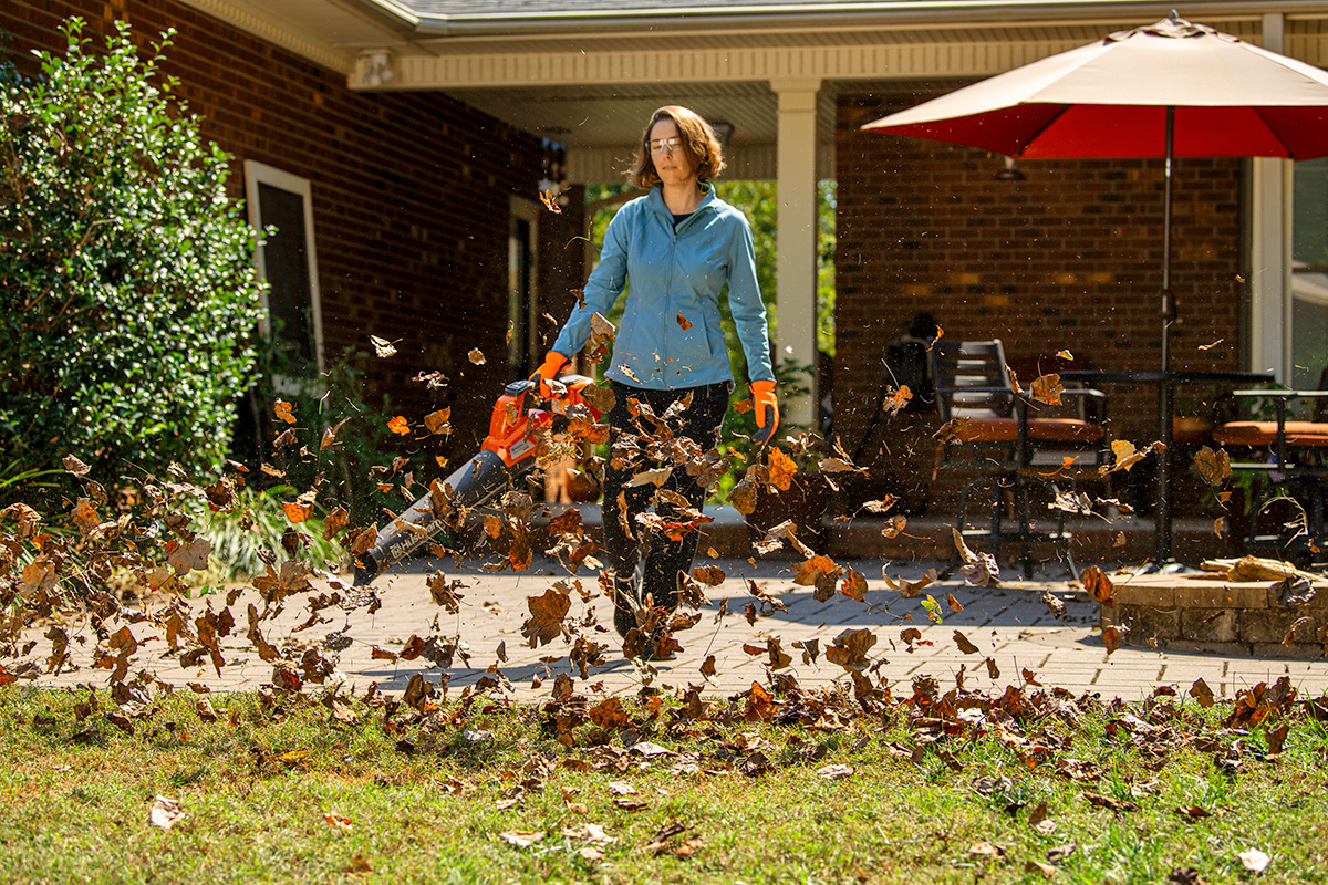 A lady using a Husqvarna leaf blower to remove leaves from her patio.