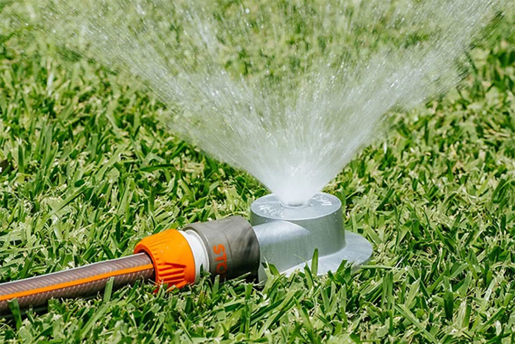 An aluminium Neta fountain spray watering green grass.